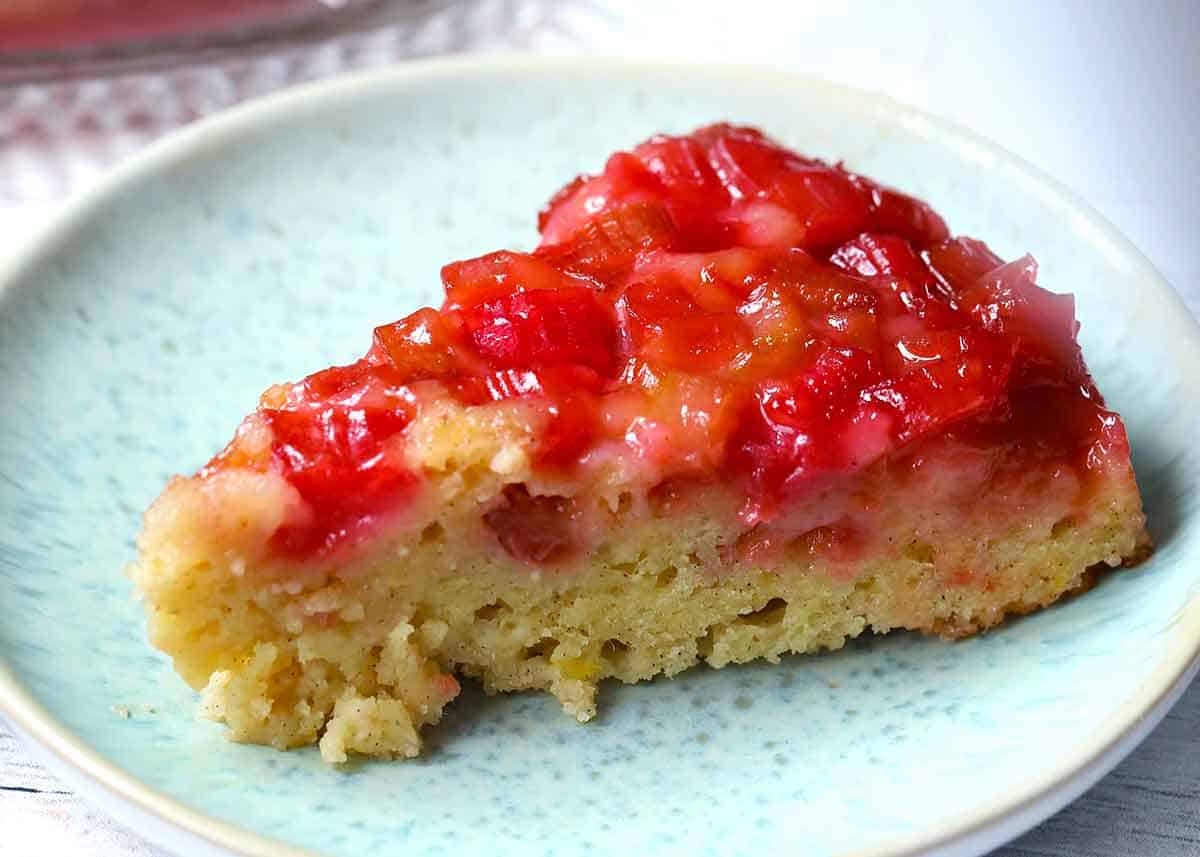 A close up photo of a side view of a slice of upside down rhubarb cake on a blue plate.