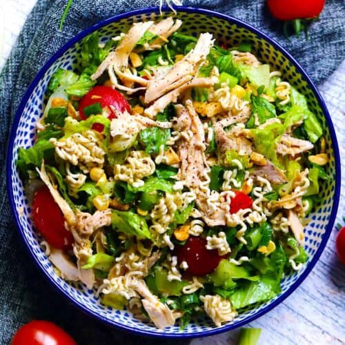 Square photo of overhead shot of a salad with crushed up Ramen noodles in it, in a blue patterned bowl.