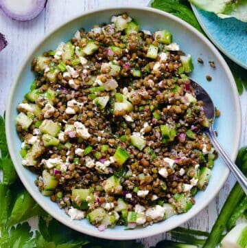 Square overhead photo of Greek lentil salad with lentils, cucumber, feta cheese, celery, and red onion in a blue bowl with a spoon.