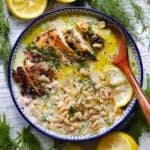 Square overhead photo of a broth bowl with sliced broiled chicken, orzo, and lemon avgolemono broth, garnished with dill and lemon slices.