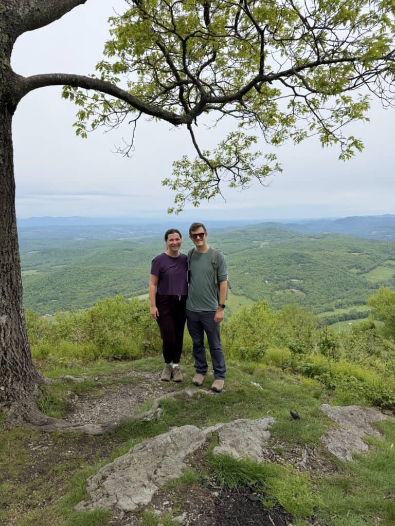 Food blogger Elizabeth Lindemann and her husband Zach on a hike, posing at the top of a mountain in Vermont with a vista in the background.